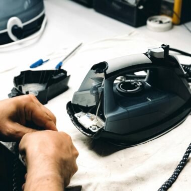 Hands working on repairing an iron in a workshop. Tools and parts are visible.